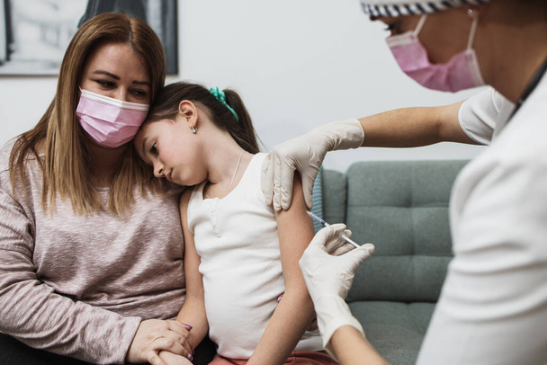 Female doctor vaccinating child patient during home visit. Coronavirus or Covid-19 pandemic prevention and protection concept. - Foto, afbeelding