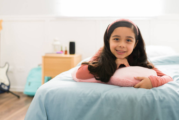 Πορτρέτο ενός όμορφου Λατίνου μικρού κοριτσιού που χαμογελά ενώ χαλαρώνει στην κρεβατοκάμαρά της κατά τη διάρκεια μιας ημέρας αναψυχής   - Φωτογραφία, εικόνα