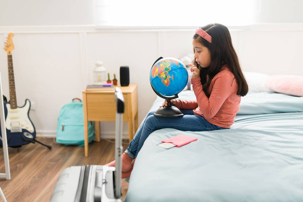 Profil d'une petite fille intelligente apprenant sur les pays dans sa chambre à coucher tout en utilisant un globe avant de partir en vacances - Photo, image