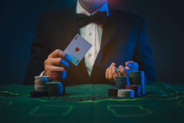 Adam satıcı ya da krupiye, elinde iki iskambil kâğıdı olan bir kumarhanenin arka planındaki poker kartlarını karıştırıyor. Kumarhane, poker, poker konsepti - Fotoğraf, Görsel