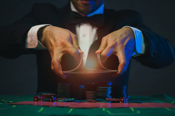 Άντρας έμπορος ή κρουπιέρης ανακατεύει τα χαρτιά του πόκερ σε ένα καζίνο στο παρασκήνιο ενός τραπεζιού, asain άνθρωπος κρατώντας δύο τραπουλόχαρτα. Καζίνο, πόκερ, πόκερ έννοια παιχνιδιού - Φωτογραφία, εικόνα