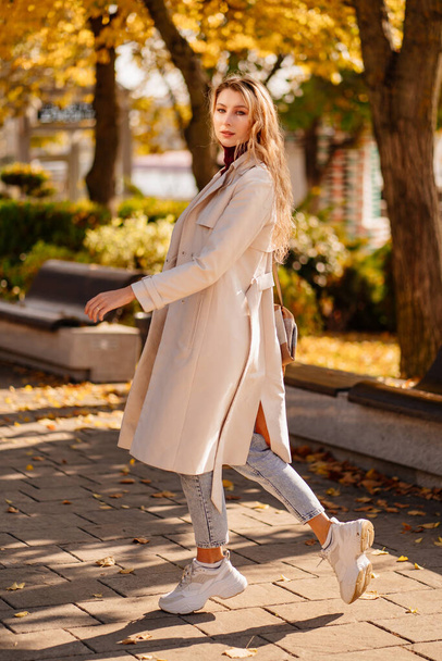 beautiful blonde student or businesswoman in a coat walks down an autumn street. - Fotografie, Obrázek
