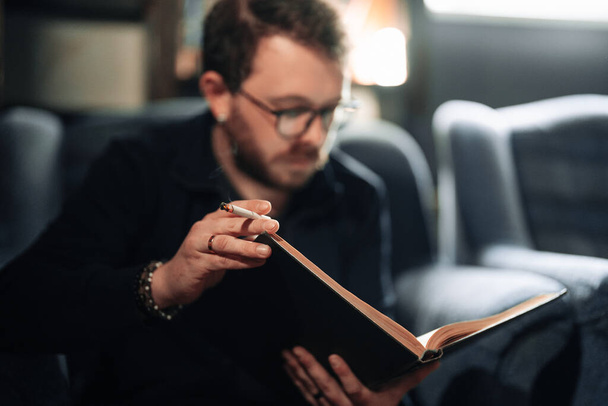 Estudiante adulto leyendo un libro en la biblioteca de la universidad mientras fuma - Foto, imagen