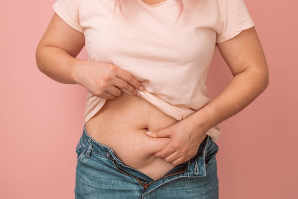 Kobieta trzyma nadmiar tłuszczu w brzuchu, koncepcja nadwagi. Nadwaga samica w dżinsach - Zdjęcie, obraz