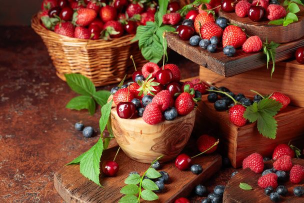 Assorted fresh berries with leaves. Strawberries, raspberries blueberries, and sweet cherries on an old vintage table.  - 写真・画像