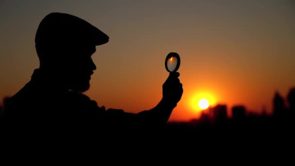 Silhouette masculine détective au coucher du soleil en utilisant une loupe - Séquence, vidéo