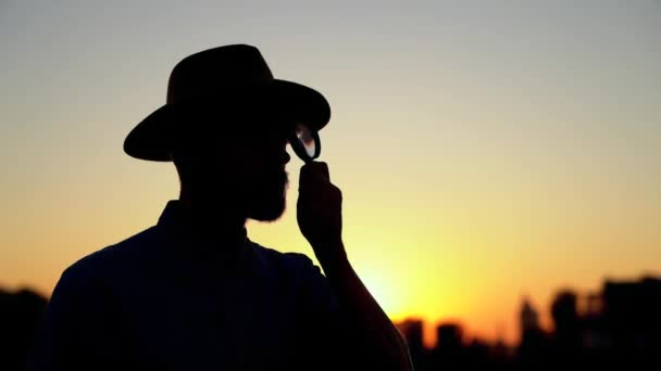 Człowiek w kapeluszu jak sylwetka patrząc za pomocą szkła powiększającego - Materiał filmowy, wideo
