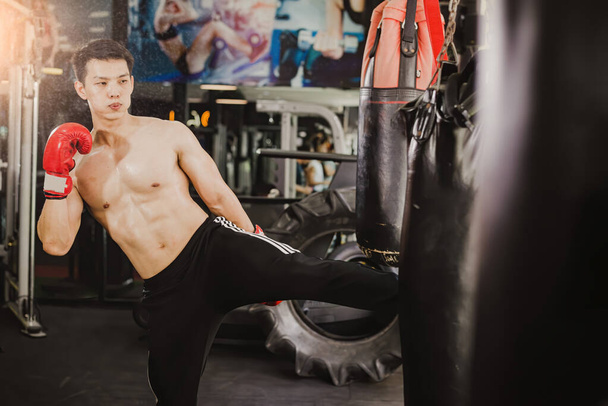 Fitness edzés koncepció, jóképű jóképű férfi csinál boksz gyakorlat rugdossa homokzsákok és mutatja ki az izmait. - Fotó, kép