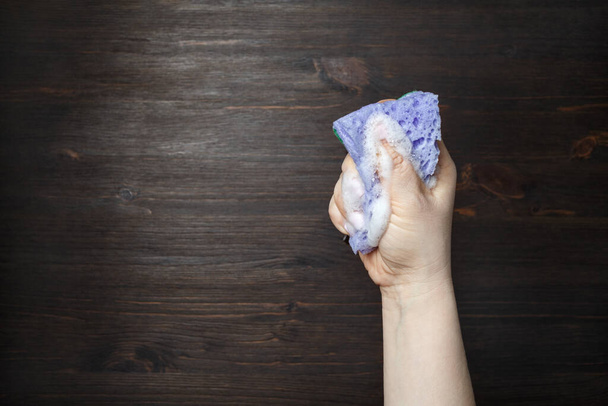 Hand and kitchen sponge in soapsuds on wooden background. Copy space. Place for your text. - Fotó, kép