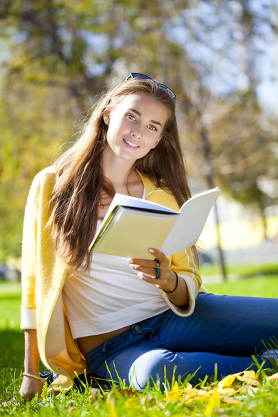 Beautiful schoolgirl sitting in autumn park and reading a book - Fotó, kép