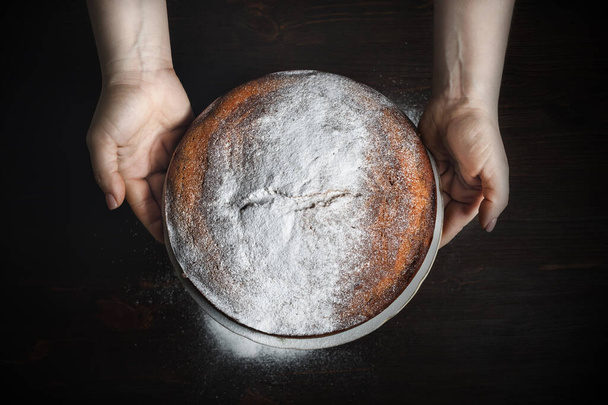 Cake decorated with powdered sugar in female hands. Icing sugar sprinkled on pie. Bon Appetit. - Foto, Imagen