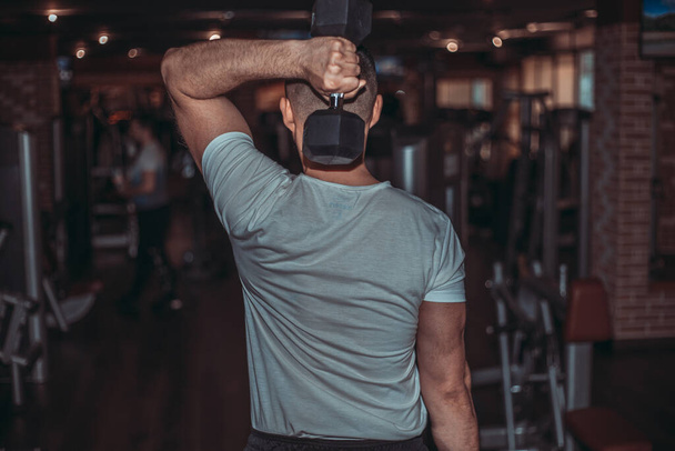 Jongeman bodybuilder doet workout met zware halter in donkere sportschool. - Foto, afbeelding