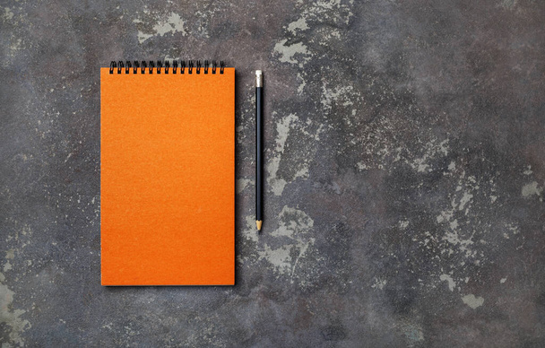 Φωτογραφία από κενό πορτοκαλί μπλοκ και μολύβι σε μπετόν φόντο. Αντιγραφή χώρου για κείμενο. Επίπεδη. - Φωτογραφία, εικόνα