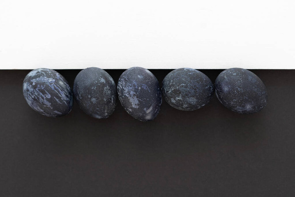 青いイースターエッグ黒を背景に白を背景にしたテキストトップビュー、イースターミニマリズム黒と白 - 写真・画像