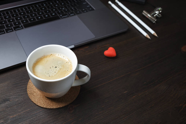 Kaffeepause-Konzept. Kaffeetasse, Laptop, Radiergummi in Herzform und Bleistifte auf Holzgrund. Selektiver Fokus. - Foto, Bild