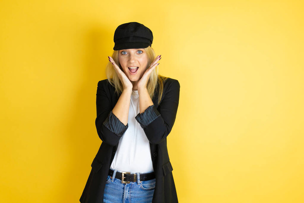 Beautiful woman wearing casual white t-shirt and a cap over isolated yellow background crazy and scared with hands on head, afraid and surprised of shock - Fotoğraf, Görsel