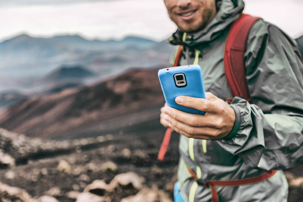 Phone man texting during trek hike in volcano mountain. Young person on travel lifestyle using his smartphone online - Фото, изображение