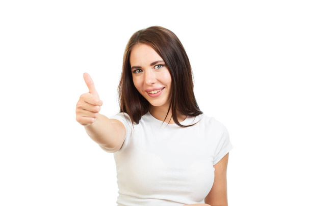 Cute girl with brown hair in a white T-shirt shows a thumbs up gesture. - Φωτογραφία, εικόνα