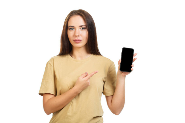 Młoda dziewczyna wskazuje palcem na czarny ekran smartfona. Izolacja na białym tle. - Zdjęcie, obraz