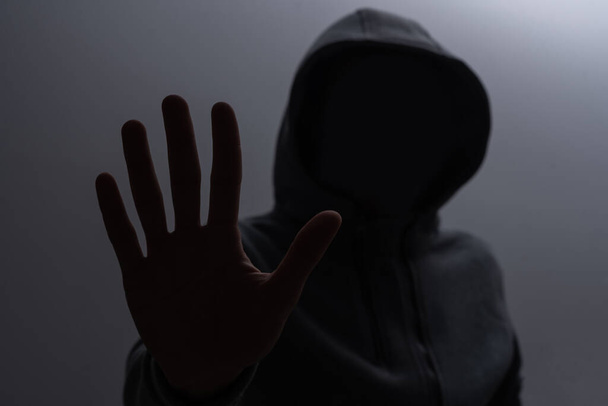 Silhouette de l'homme dans le capot ou hooligan sur fond sombre avec espace de copie - Photo, image