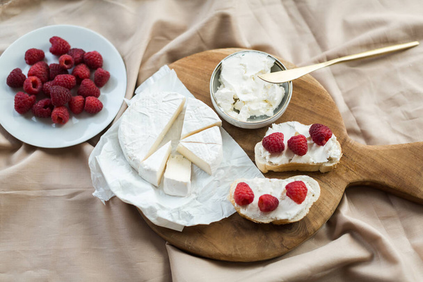 aesthetic breakfast camembert, bruschetta with cream cheese and raspberries on a wooden board - Fotoğraf, Görsel