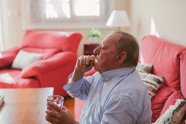 an elderly man taking a pill in his home - Photo, Image