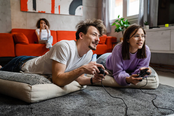 人々のグループ白人家族男性と女性母親と父親と子供の女の子と床に横たわっ家庭用ゲーム機でジョイスティックやコントローラーを使用してゲーム機幸せな笑顔を持っている現実の人々 - 写真・画像