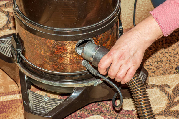Il processo di pulizia del tappeto con un aspirapolvere con un filtro dell'acqua. La mano di una donna inserisce un tubo dell'aspirapolvere nella presa d'aria. - Foto, immagini