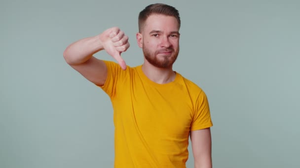 Zdenerwowany mężczyzna w luźnej koszulce pokazuje kciuki w dół znak gest, dezaprobata, niezadowolony niechęć - Materiał filmowy, wideo