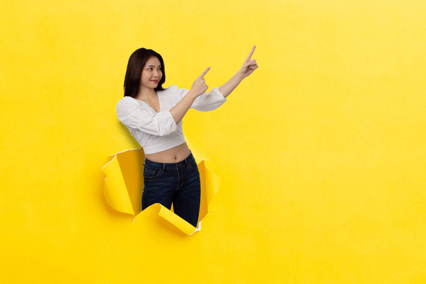 Happy Asian woman smiling with thumbs up pointing at empty space Stand on a hole in the middle of the yellow paper. - 写真・画像
