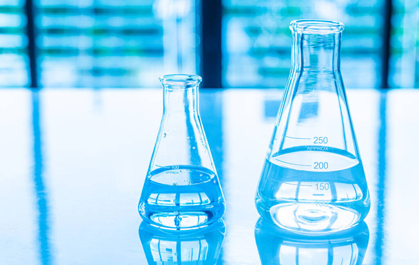 Concepto de experimento químico en laboratorio científico Dos frascos científicos de diferentes tamaños contienen diferentes productos químicos en el escritorio blanco. Nadie. Copie el espacio a la izquierda para el diseño. Fondo borroso. De cerca. - Foto, Imagen