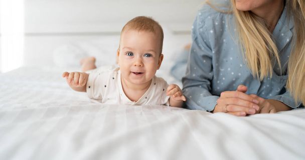 Mutlu annelik ve çocukluk kavramı. Genç bir anne, 4 aylık bir bebekle beyaz bir yatakta yatar. Parlak bir yatak odasında. Bebek bakımı, çocuk bakımı, oğluyla veya kızıyla boş zaman. - Fotoğraf, Görsel