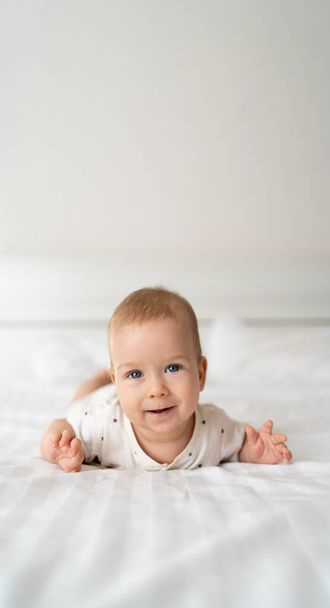 entzückend lächelndes weißes kaukasisches Mädchen mit blauen Augen, vier Monate alt, auf dem Bett liegend und in die Kamera blickend. Seitenansicht. Kindheit glücklich Lebensstil Konzept. banner - Foto, Bild