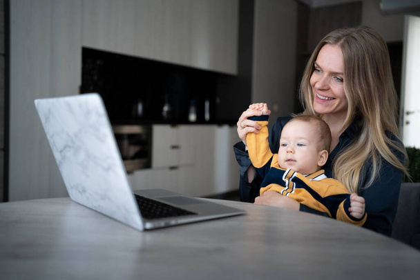 Kaukasische Mutter mit weißem Baby, die von zu Hause aus online im Internet arbeitet. Arbeitsplatz einer Freiberuflerin mit Kind. Bleiben Sie zu Hause alleinerziehende Mutter arbeiten aus der Ferne. - Foto, Bild