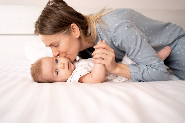 caucasian loving mom playing first games with her 8 month old baby in the bedroom, side view, maternity leave, concept of happy motherhood and childhood - Photo, Image