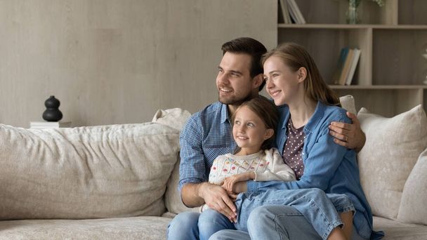 Dreamy parents and sweet daughter girl sitting on couch - Foto, imagen