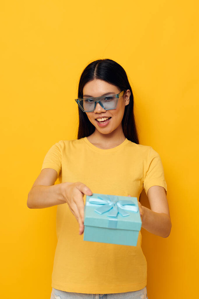 Portrait Asian beautiful young woman with a gift in glasses holiday yellow background unaltered - Foto, imagen