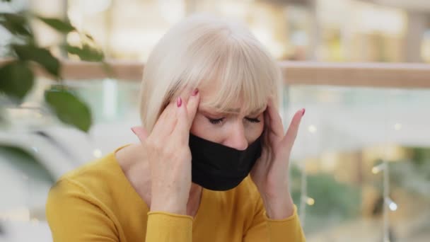 Close-up unhappy caucasian middle-aged woman in medical mask sitting indoors holding hands behind head suffering headache closing eyes feeling tired painful sensations chronic migraine health problems - Footage, Video