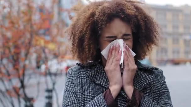 Kranke Afrikanerin mit lockigem Haar bläst laufende Nase in Seidenpapier im Freien Erkältungsallergien Atemwegsvirus Mädchen leidet an ansteckender Rhinitis Symptom Herbst in der Stadt Grippe-Pandemie - Filmmaterial, Video