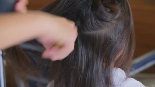 Menina asiática recebe seu cabelo seco em um salão de beleza por um cabeleireiro. Cabeleireiro faz penteados para meninas bonitos. - Filmagem, Vídeo