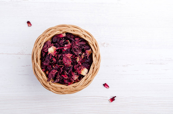 Dried hibiscus petals in a wicker basket on a light wooden background. Top view. Copy space. - Photo, image