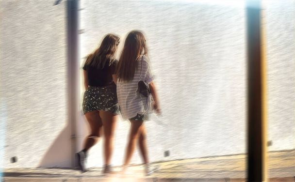太陽の光の下で壁を歩いている二人の十代の女の子 - 写真・画像