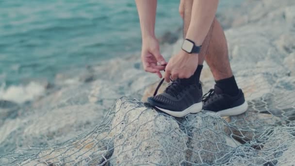 Férfi sportos kötött kocogó cipő készen áll a futás a szabadban a tengerparton. Jóképű férfi gyakorolja a kora reggeli napfelkeltét.. - Felvétel, videó
