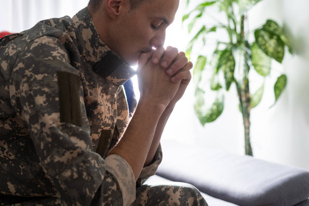 Soldado triste de uniforme cobrindo sua boca enquanto sentado em um sofá
 - Foto, Imagem