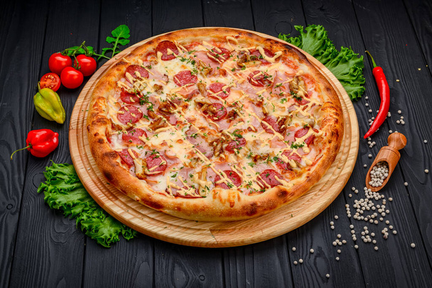Tasty pepperoni pizza and cooking ingredients tomatoes basil on black concrete background. Top view of hot pepperoni pizza. With copy space for text. Flat lay - 写真・画像