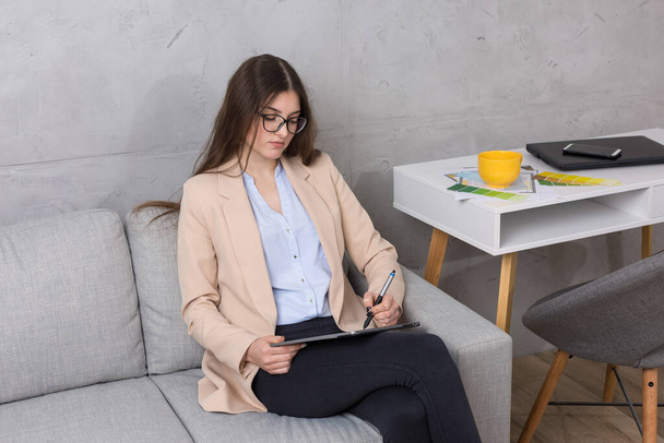 Una giovane designer seduta su un divano disegna su un tablet. Fa calcoli di affari sul computer. - Foto, immagini