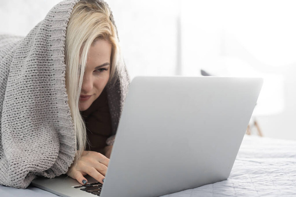 vrouw met laptop bedekt met deken in de slaapkamer - Foto, afbeelding