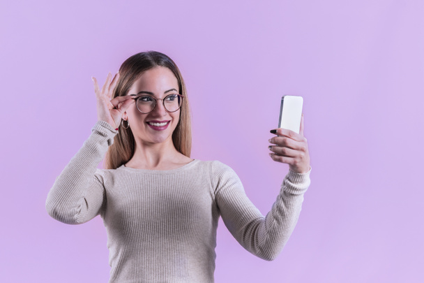 Νεαρή γυναίκα με γυαλιά ελέγχει το τηλέφωνό της - Φωτογραφία, εικόνα