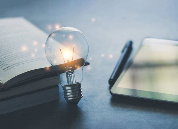 Bright light bulb with book or text book and tablet with copy space. Business and education idea concept of learning inspiration and knowledge cognition. - Photo, Image