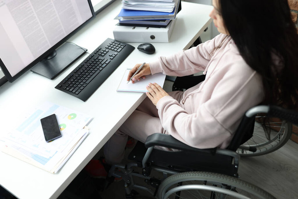 Disabled woman in wheelchair with documents uses computer - Foto, imagen
